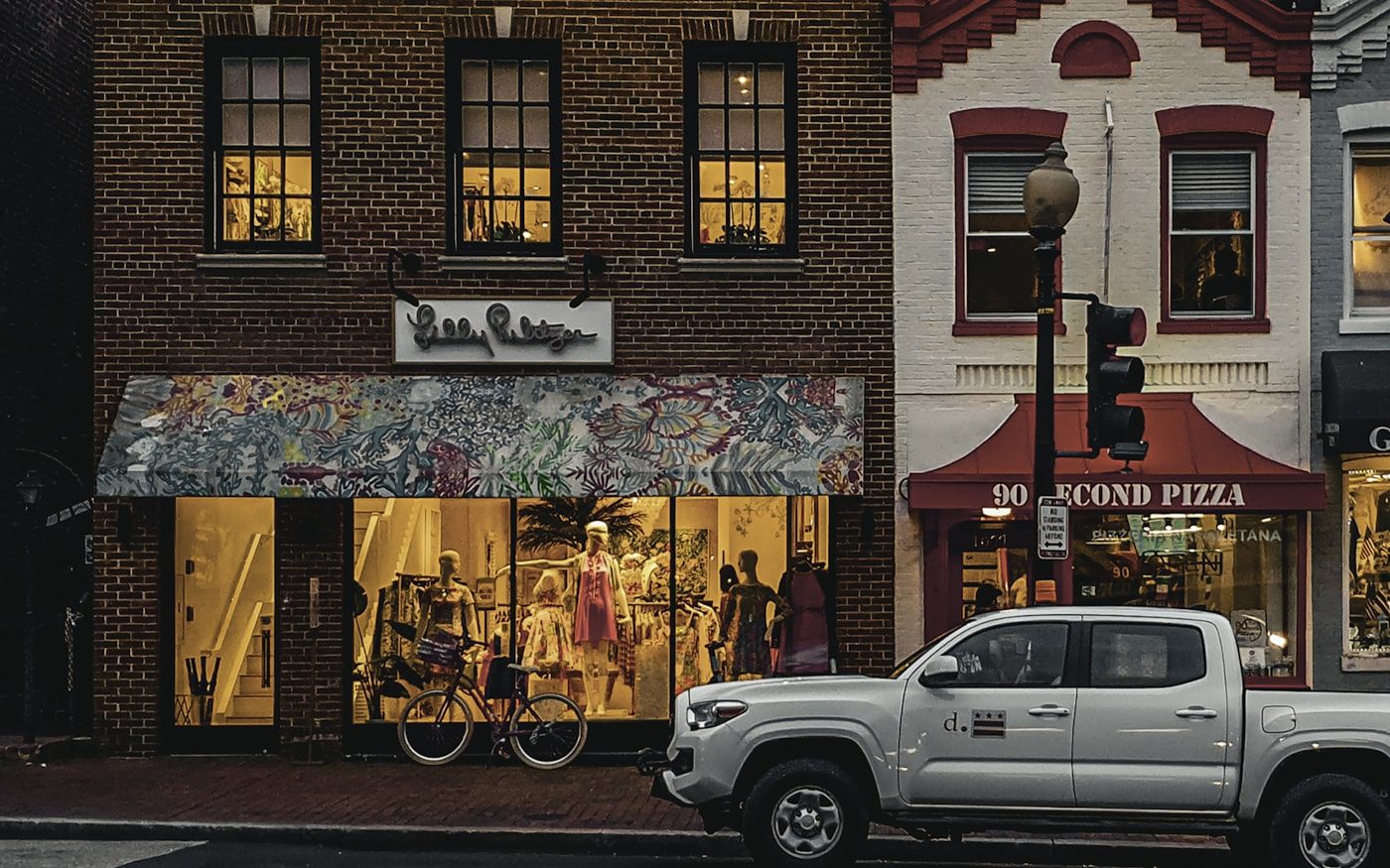 Shopfronts and a parked pickup truck on a small-town main street at dusk